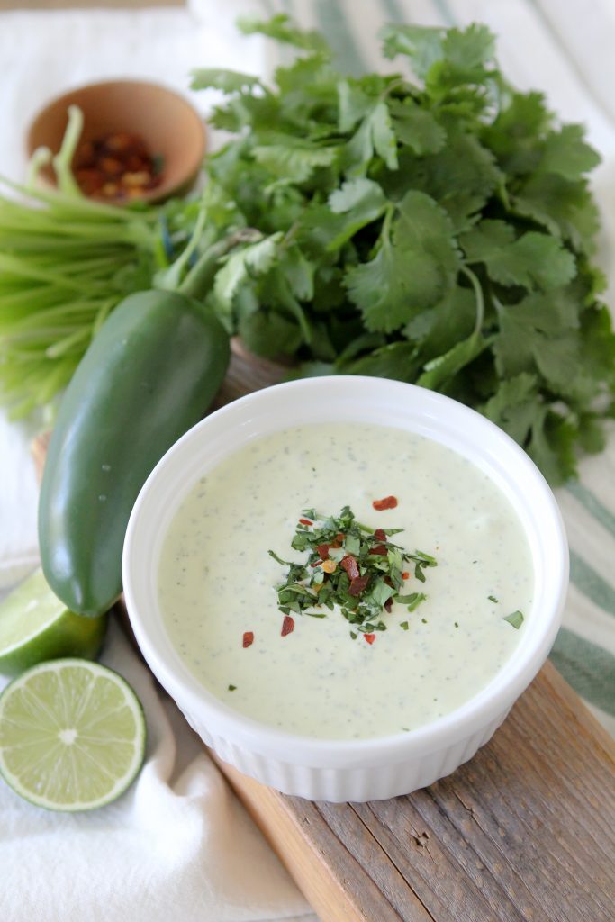 a small bowl of whole30 green sauce on a chopping board surrounded with ingredients for green sauce recipe