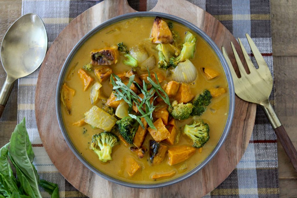 Vegan Pumpkin Curry with chunks of roasted sweet potatoes served in a blue bowl placed on a wooden board 