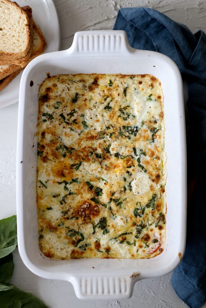 a white casserole dish with baked eggs, basil and tomatoes