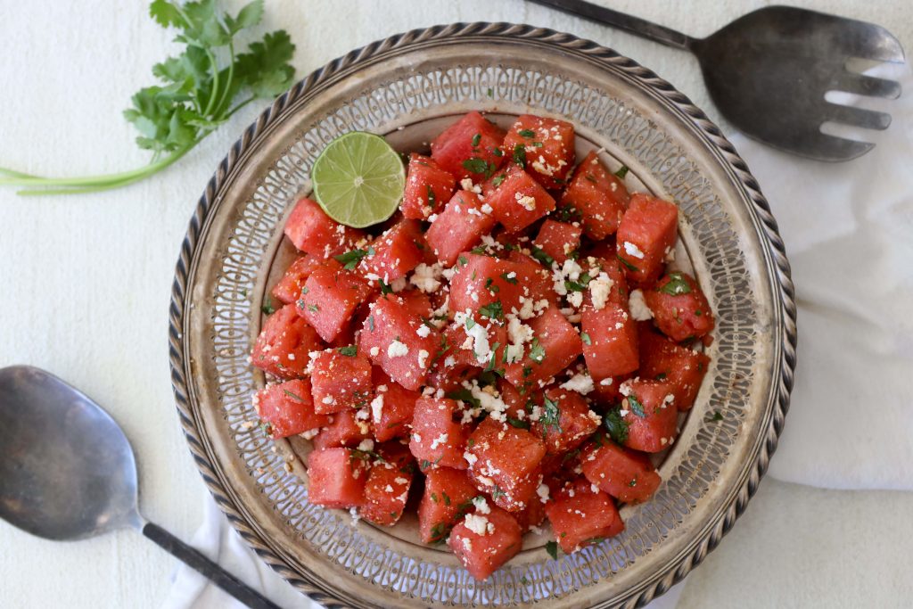 a big metal plate with chili lime watermelon salad topped with queso fresco and chopped herbs