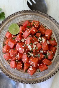 chili lime watermelon salad topped with queso fresco on a metal plate