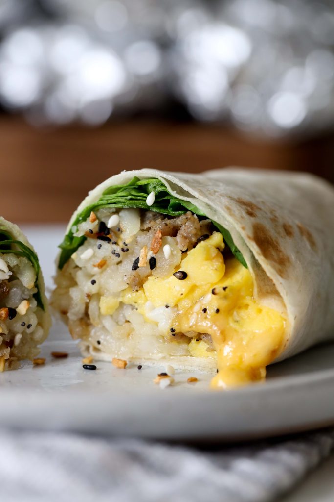 side view of a halved healthy gluten-free everything bagel breakfast burrito with sausage and cheese 